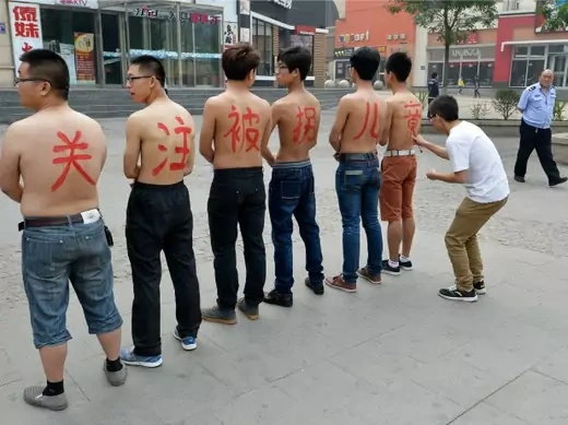 A security guard (R) looks on as a man writes characters on the back of six topless activists with the message "pay attention to children trafficking" during a demonstration against children abduction and trafficking, in Taiyuan, Shanxi province May 18, 2013. REUTERS/Jon Woo (CHINA - Tags: CRIME LAW SOCIETY)