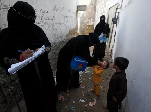 A polio vaccinator administers polio vaccine drops to a boy while a colleague takes notes nearby in Karachi, Pakistan, October 2014 (Courtesy Reuters/Akhtar Soomro).