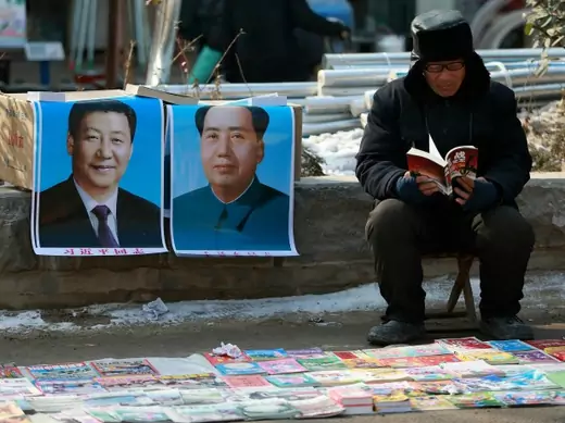 A book vendor reads a book as he waits for customer next to portraits of Chinese President Xi Jinping (L) and late Chairman Mao Zedong, at an open-air fair in Juancheng county, Shandong province January 30, 2015. REUTERS/Stringer (CHINA - Tags: SOCIETY POLITICS) CHINA OUT. NO COMMERCIAL OR EDITORIAL SALES IN CHINA