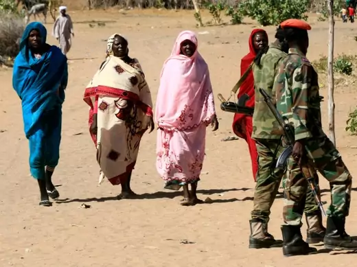 Military personnel walk past women in Tabit village in North Darfur, Sudan. The joint peacekeeping mission in the region known as UNAMID visited Tabit in November 2014 to investigate media reports of an alleged mass rape of 200 women and girls (Courtesy Mohamed Nureldin Abdallah/Reuters). 