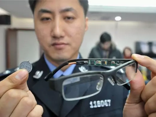 A police officer displays a pair of glasses (R) with a hidden camera and a tiny receiver attached to a coin, which are both exam cheating equipment confiscated by the police, in Shenyang, Liaoning province November 22, 2013. Chinese authorities vowed harsh treatment for organizing or helping cheating in the national college entrance exam, which took place on June 7 and 8 this year. Education and police authorities will continue to investigate crimes including stealing and selling examination papers, leakin