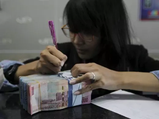 A money changer prepares Indonesian rupiah for a customer in Jakarta