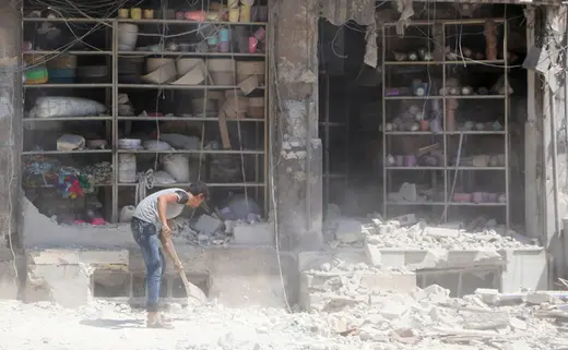 A civilian removes the rubble in front of a damaged shop after an airstrike in the rebel held al-Saleheen neighborhood of Aleppo.