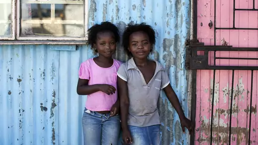 Girls stand outside shacks made from metal in Cape Town's Khayelitsha township.