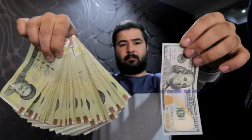 A money changer in Tehran poses with a U.S hundred dollar bill and the amount being given when converting it into Iranian rials.