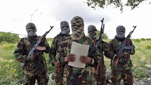 A military spokesman for al-Shabaab issues a statement in front of several fighters bearing arms. 