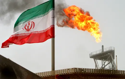 A gas flare on an oil production platform is seen alongside an Iranian flag in the Gulf July 25, 2005. 