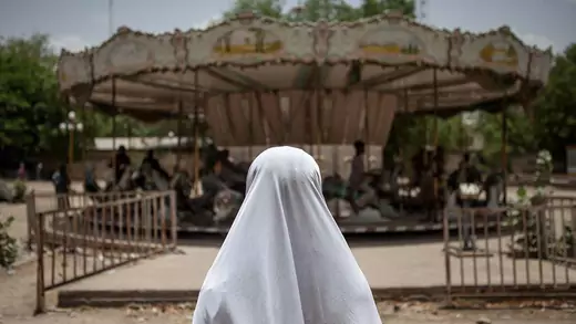 A girl watches other children on a merry-go-round in an abandoned amusement park in Maiduguri, Nigeria.