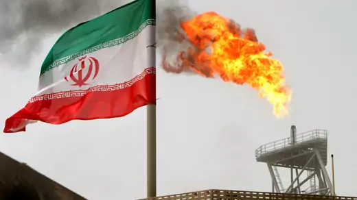 A gas flare on an oil production platform in the Soroush oil fields is seen alongside an Iranian flag in the Persian Gulf, Iran, July 25, 2005.