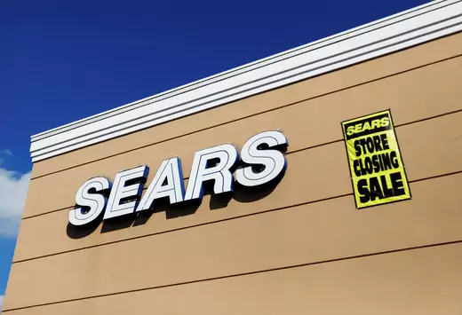 A store closing sale sign is posted next to a Sears logo in New Hyde Park, New York.