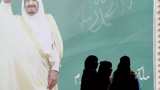 Women walk past a poster of Saudi Arabia's King Salman bin Abdulaziz Al Saud.