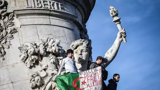  Algerian protesters in Paris hold a sign reading, "System get out, free Algeria."