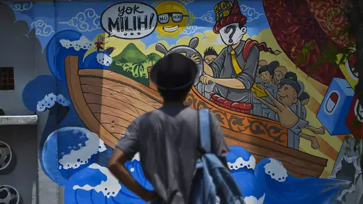 A man stands in front of an Indonesian election campaign mural