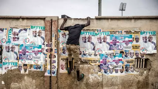 A young man climbs up a wall plastered with election posters during a rally in Kano to celebrate President Muhammadu Buhari’s reelection.