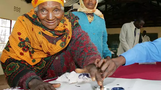 An election official helps a Kenyan woman cast her vote at a polling station in Nyeri district, Kenya, November 21, 2005.