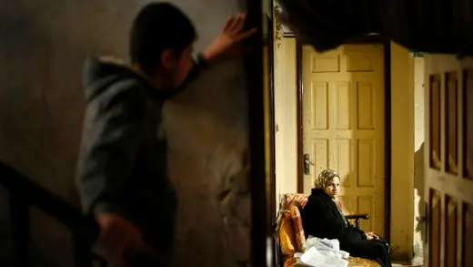 A boy looks on as a Palestinian woman suffering from cancer sits inside her home.