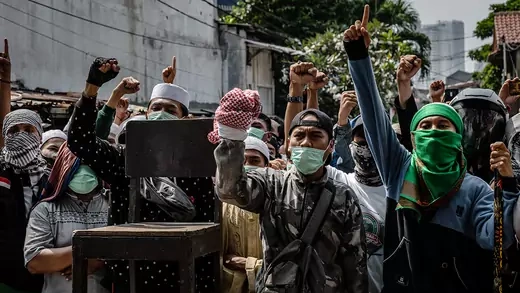 Protesters wearing medical masks hold their first in the air during a demonstration in Jakarta.