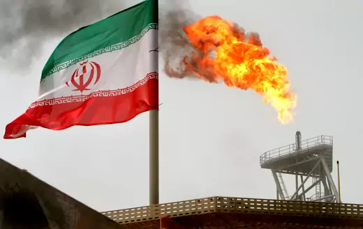 A gas flare on an oil production platform in the Soroush oil fields is seen alongside an Iranian flag in the Persian Gulf, Iran, July 25, 2005. 