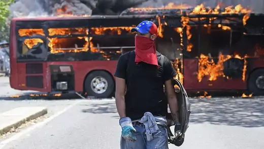 An opposition demonstrator walks near a bus in flames during clashes with soldiers loyal to Venezuelan President Nicolas Maduro in the surroundings of La Carlota military base in Caracas on April 30, 2019.