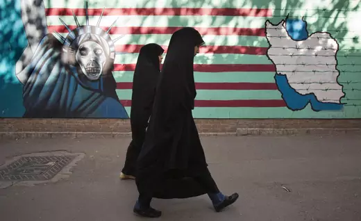 Two Iranian women walk past a mural in Tehran.