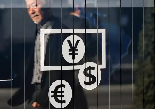 Passers-by are reflected on a signboard displaying currency signs outside a bank in Tokyo November 27, 2014. REUTERS/Issei Kato/File Photo
