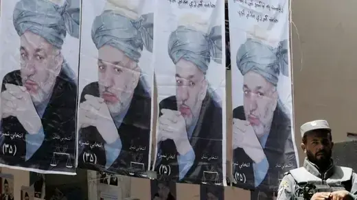 An Afghan policeman sit in front of campaign posters of Hamid Karzai. 
