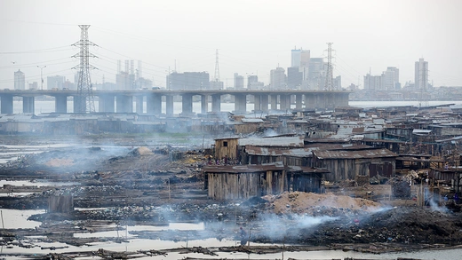 A slum with a bridge, electric transmission lines, and a high-rises in the background.