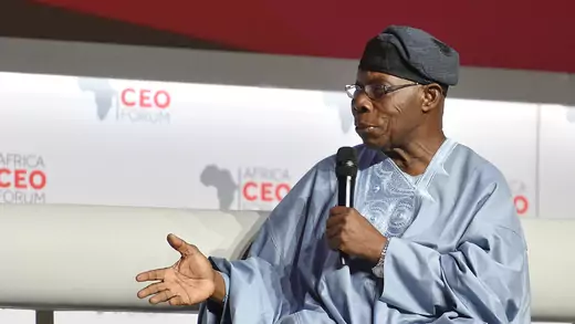 Former President Obasanjo speaks into a microphone while seated on stage at the Africa CEO forum.