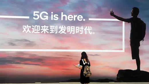 A woman walks past a billboard reading '5G is here' on day one of the Mobile World Congress (MWC) Shanghai 2019 at the Shanghai New International Expo Center on June 26, 2019 in Shanghai, China.