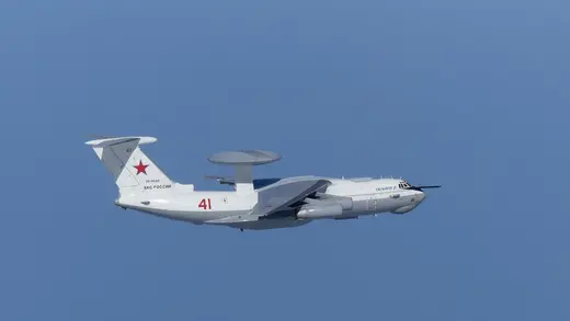 A white military plane flies in a blue sky.