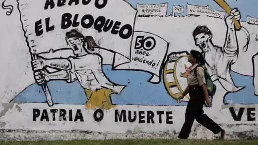 A woman walks beside a mural that reads, "Down with the blockade" in Havana.