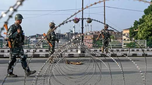 Three Indian troops stand near a barbed wire road block in Jammu and Kashmir.