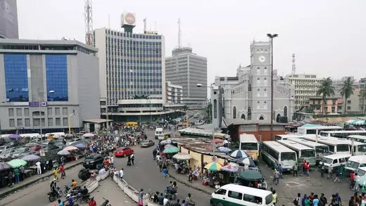 People, buses, and motorbikes move along roads on Victoria Island, Lagos, Nigeria in front of skyscrapers.