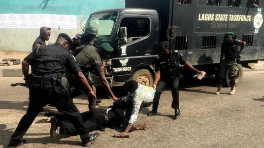 Police officers pull two people on the ground next to a truck that says "Lagos State Taskforce."
