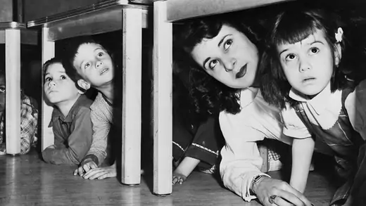 School children and their teacher peer from beneath the table during New Jersey's first state-wide air raid test.