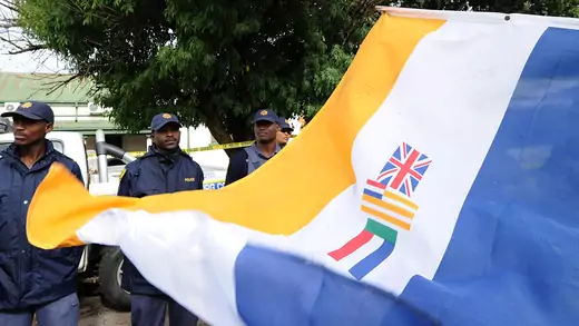 South Africa's apartheid-era flag flutters in front of three black police officers.