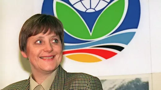 Angela Merkel smiles in front of a colorful climate summit logo. 