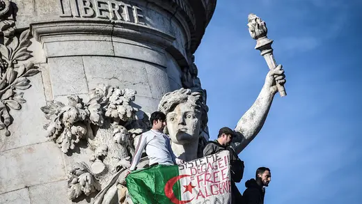 Algerian protesters in Paris hold a sign reading, “System get out, free Algeria.”