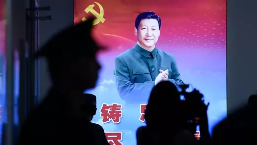 Shadows of people are seen in front of an illuminated poster of Xi Jinping.