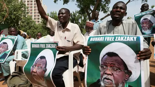 Protesters sit and hold posters that say "Buhari Free Zakzaky."