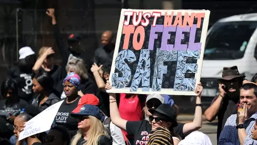 Demonstrators hold signs, one of which reads "Just Want to Feel Safe."