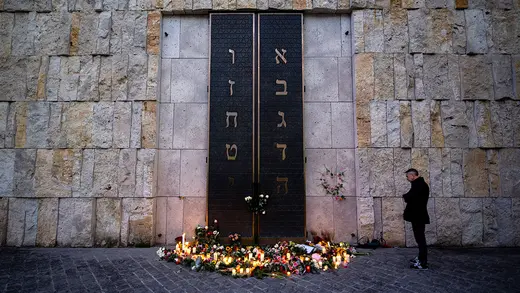 A man stands at the door of the Munich synagogue next to flowers and candles. 