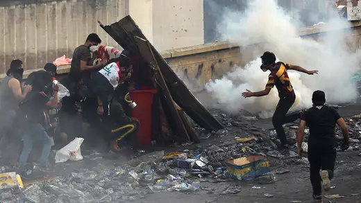 Iraqi anti-government protesters stand behind a barricade as security forces fire tear gas to keep demonstrators from storming the Green Zone, which hosts government offices and foreign offices, on October 28, 2019 in Baghdad