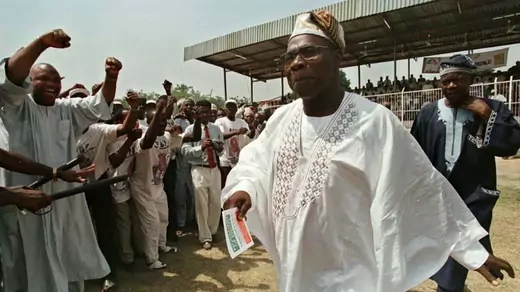 Obasanjo walks past a cheering crowd in a white robe.