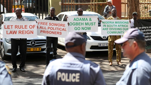 Police officers look on as Nigerians living in South Africa hold placards in protest against President Muhammadu Buhari.