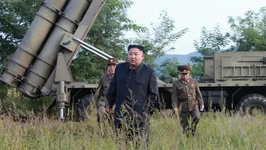 North Korean leader Kim Jong-un walks through a field with two military officials. 
