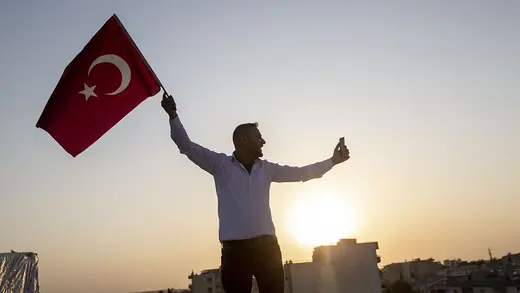 A man waves a Turkish flag as the sun sets behind him. 