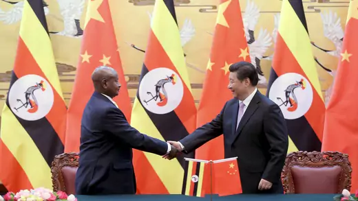 Ugandan President Yoweri Museveni shakes hands with Chinese President Xi Jinping flanked by Chinese and Ugandan flags.