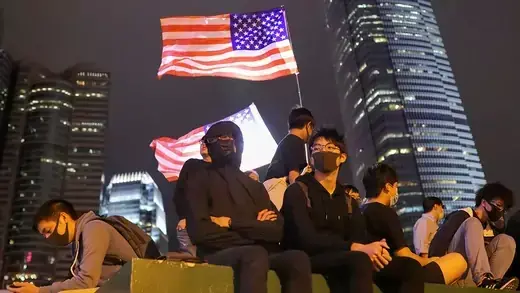 People dressed in black sit by a U.S. flag in Hong Kong. 