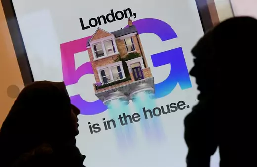 Pedestrians walk past an advertisement promoting the 5G data network at a mobile phone store in London